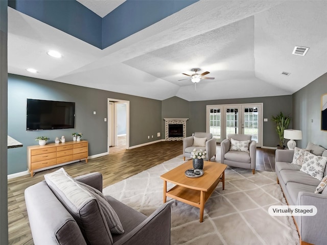 living room with a stone fireplace, a textured ceiling, wood-type flooring, ceiling fan, and lofted ceiling