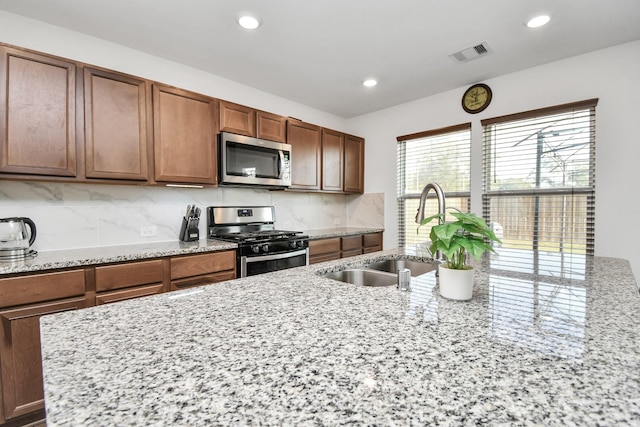 kitchen featuring sink, light stone counters, appliances with stainless steel finishes, and tasteful backsplash