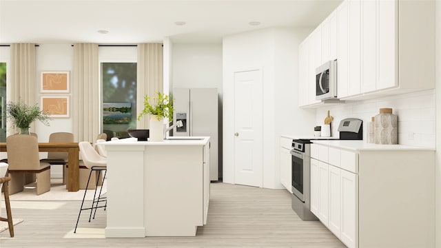 kitchen featuring white cabinetry, stainless steel appliances, backsplash, a kitchen breakfast bar, and light hardwood / wood-style flooring