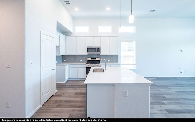 kitchen featuring decorative light fixtures, tasteful backsplash, a kitchen island with sink, appliances with stainless steel finishes, and white cabinets