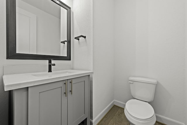 half bath with baseboards, vanity, toilet, and wood finished floors