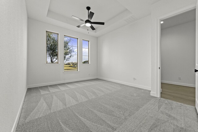 carpeted empty room with ceiling fan and a raised ceiling