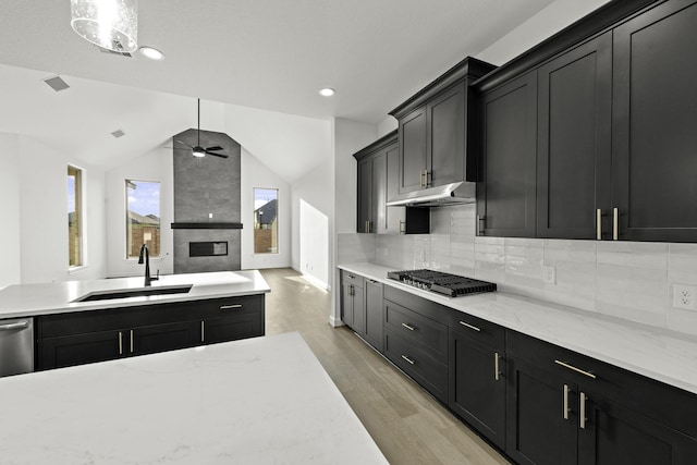 kitchen with dark cabinets, stainless steel gas cooktop, under cabinet range hood, a sink, and light stone countertops