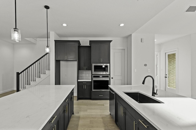 kitchen with light wood finished floors, visible vents, appliances with stainless steel finishes, a sink, and light stone countertops