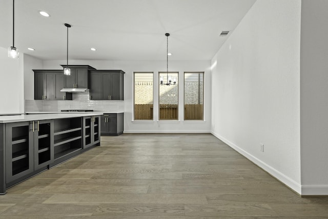 kitchen featuring under cabinet range hood, baseboards, light countertops, decorative backsplash, and light wood finished floors