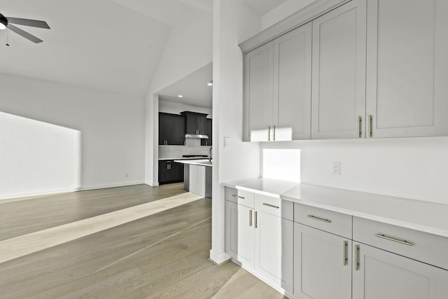 kitchen with under cabinet range hood, a ceiling fan, vaulted ceiling, light countertops, and light wood-type flooring