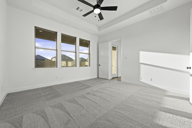 spare room with carpet flooring, a raised ceiling, visible vents, and baseboards