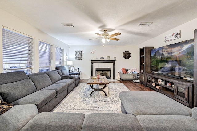 living room featuring ceiling fan, dark wood-type flooring, a textured ceiling, and a tiled fireplace