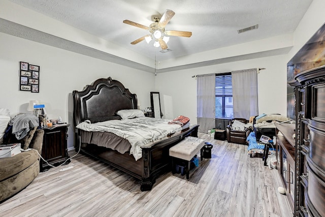 bedroom with ceiling fan, light wood-type flooring, a tray ceiling, and a textured ceiling