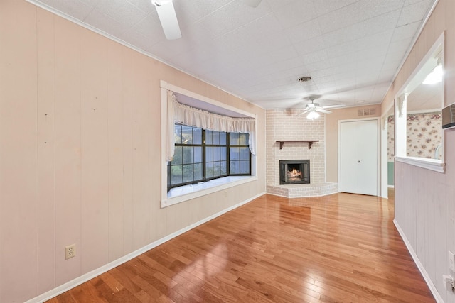 unfurnished living room with ceiling fan, wood-type flooring, wood walls, and a fireplace