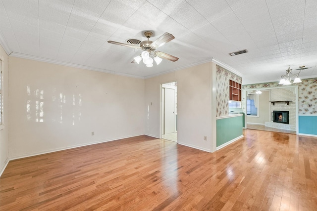 unfurnished living room with hardwood / wood-style flooring, a brick fireplace, crown molding, and ceiling fan with notable chandelier