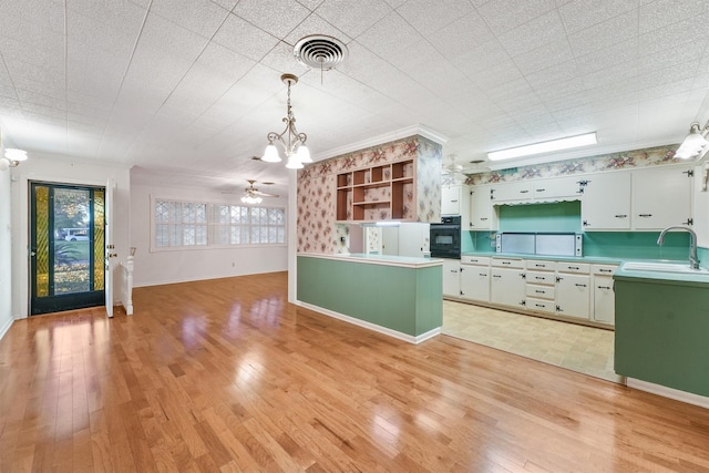 kitchen with pendant lighting, white cabinetry, light hardwood / wood-style floors, sink, and oven