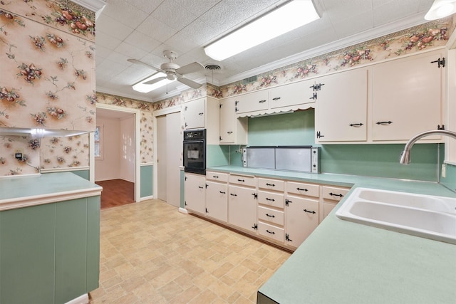 kitchen with white cabinets, black oven, sink, ornamental molding, and ceiling fan