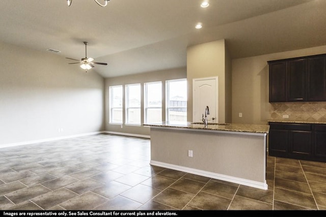 kitchen featuring lofted ceiling, ceiling fan, tasteful backsplash, a center island with sink, and sink