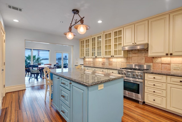 kitchen featuring pendant lighting, a kitchen island, decorative backsplash, stone countertops, and high end stove