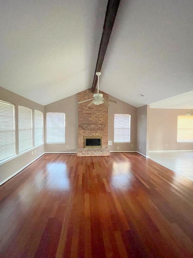 unfurnished living room featuring ceiling fan, a fireplace, lofted ceiling with beams, hardwood / wood-style flooring, and a healthy amount of sunlight