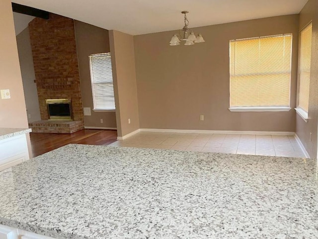 unfurnished living room with a brick fireplace, light tile patterned floors, and a notable chandelier