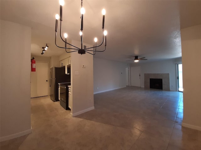 unfurnished living room featuring a tiled fireplace and ceiling fan with notable chandelier