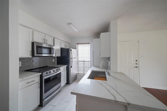 kitchen with appliances with stainless steel finishes, decorative backsplash, white cabinets, light stone counters, and sink