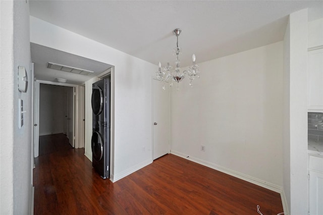 unfurnished dining area with stacked washing maching and dryer, dark hardwood / wood-style floors, and an inviting chandelier