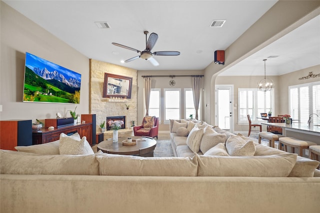 living room with ceiling fan with notable chandelier and a stone fireplace