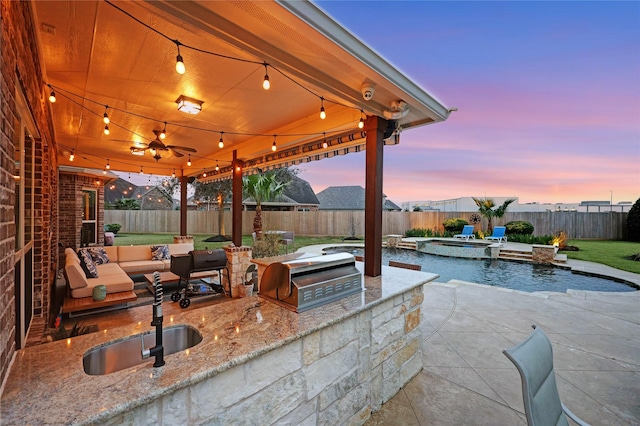 patio terrace at dusk with an outdoor kitchen, a fenced in pool, sink, and grilling area