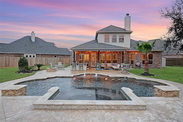 pool at dusk with an outdoor living space with a fire pit, a patio area, a yard, and an in ground hot tub