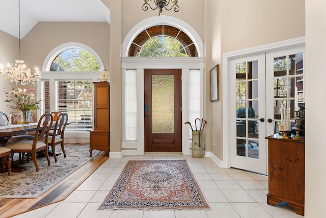 entrance foyer with high vaulted ceiling, light tile patterned floors, french doors, and a chandelier