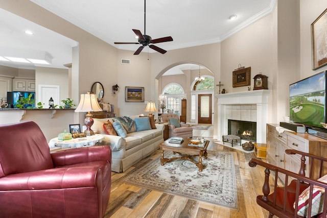 living room with light hardwood / wood-style floors, a tile fireplace, crown molding, and ceiling fan