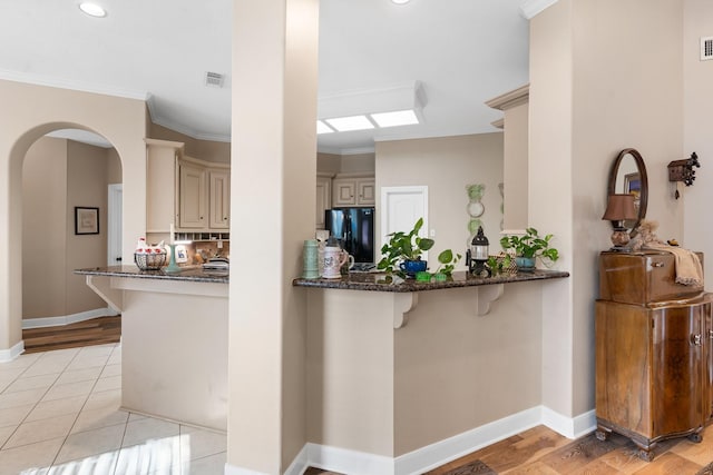 kitchen with black refrigerator, kitchen peninsula, cream cabinets, and dark stone countertops