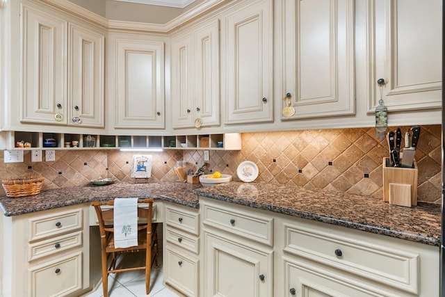 kitchen featuring built in desk, tasteful backsplash, cream cabinets, and dark stone counters