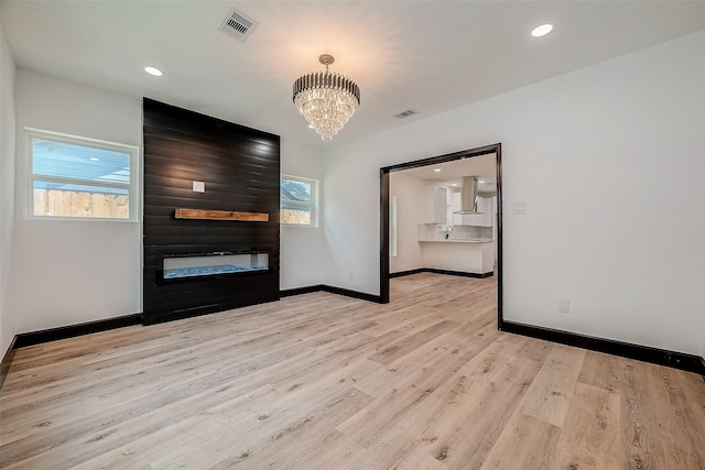 unfurnished room with light hardwood / wood-style floors, a fireplace, a chandelier, and a healthy amount of sunlight