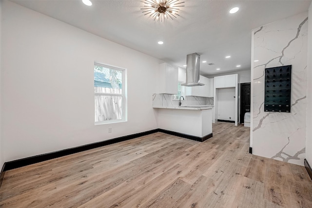 kitchen featuring white cabinets, sink, island range hood, and light stone counters