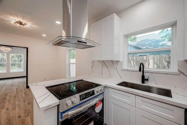 kitchen featuring white cabinets, stainless steel range with electric cooktop, sink, island range hood, and light stone counters