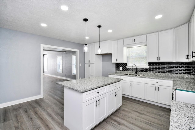 kitchen featuring light stone countertops, sink, pendant lighting, and white cabinets