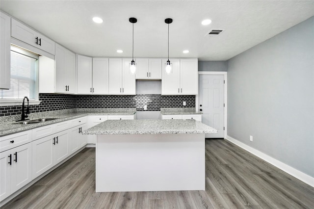 kitchen featuring light stone countertops, a center island, sink, and white cabinets