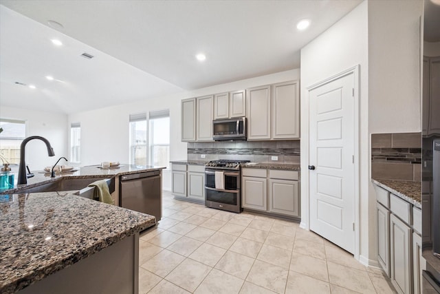 kitchen featuring gray cabinets, stainless steel appliances, backsplash, dark stone counters, and sink