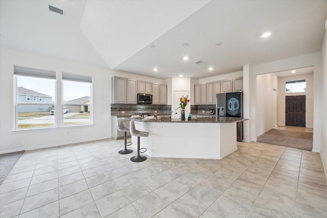 kitchen featuring lofted ceiling, dark stone countertops, a kitchen island, decorative backsplash, and stainless steel appliances