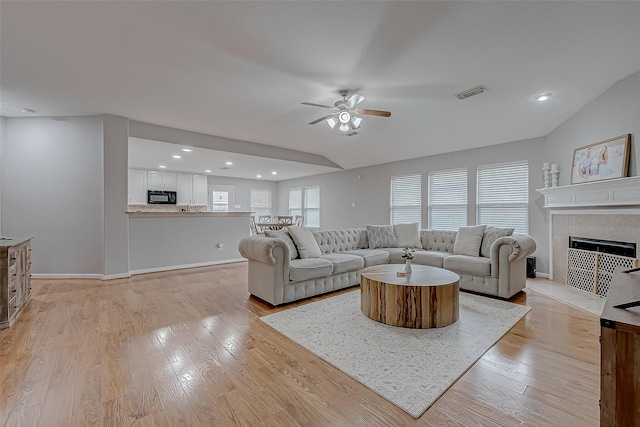 living room with ceiling fan, lofted ceiling, a tile fireplace, and light hardwood / wood-style flooring