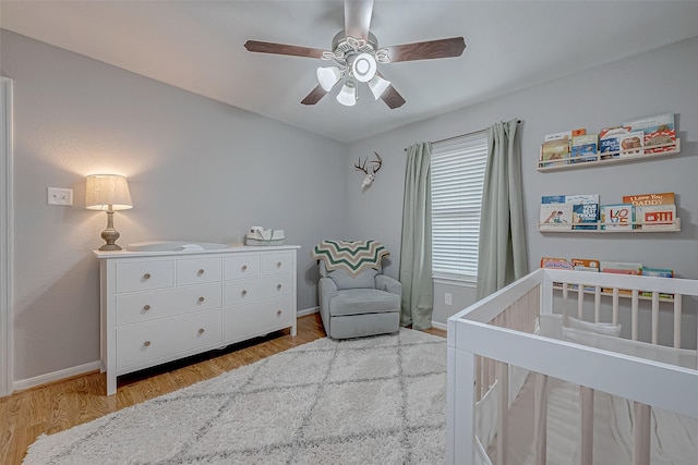 bedroom with a nursery area, ceiling fan, and light wood-type flooring