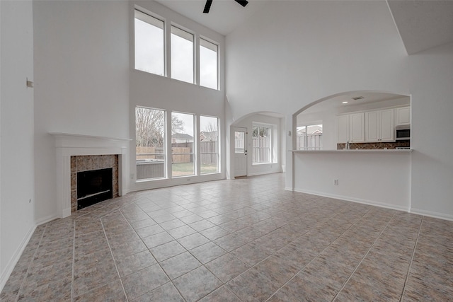 unfurnished living room featuring a tiled fireplace, light tile patterned floors, a towering ceiling, and ceiling fan