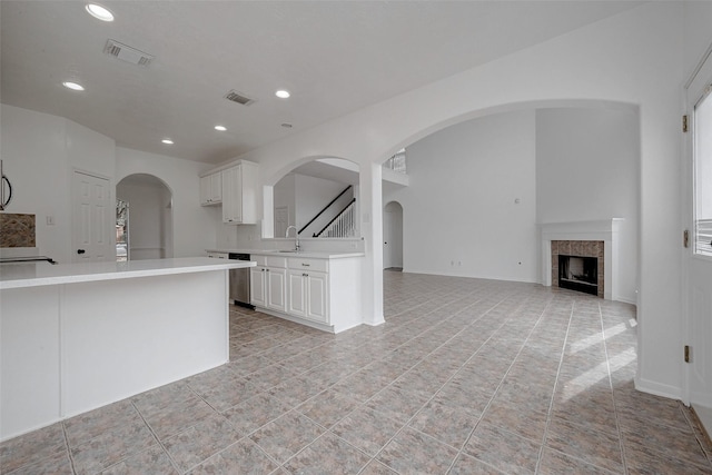 kitchen with a tile fireplace, white cabinetry, sink, stainless steel dishwasher, and light tile patterned floors