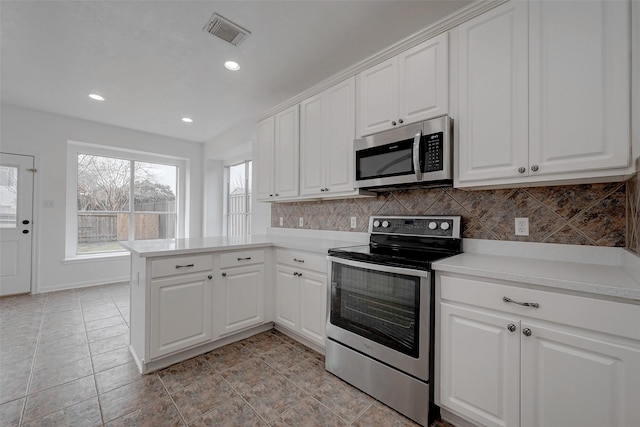 kitchen featuring appliances with stainless steel finishes, white cabinetry, backsplash, light tile patterned floors, and kitchen peninsula