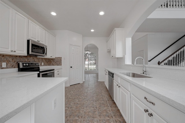 kitchen with sink, stainless steel appliances, light stone countertops, decorative backsplash, and white cabinets