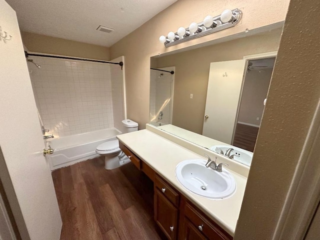 full bathroom featuring hardwood / wood-style floors, tiled shower / bath combo, a textured ceiling, vanity, and toilet