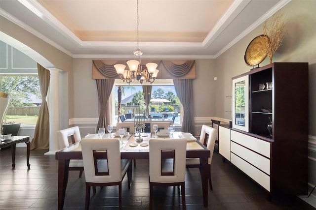 dining room with a raised ceiling, dark wood-type flooring, crown molding, and an inviting chandelier