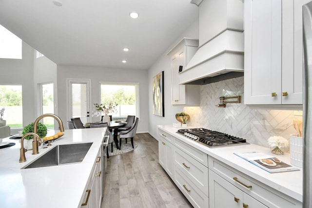 kitchen featuring premium range hood, white cabinets, stainless steel gas stovetop, and sink