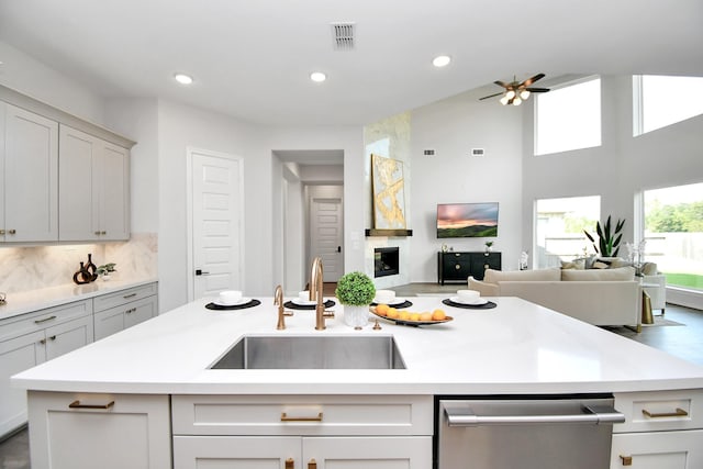 kitchen with dishwasher, a kitchen island with sink, backsplash, and sink