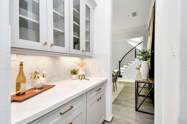 bar featuring backsplash, white cabinets, ornamental molding, and light wood-type flooring