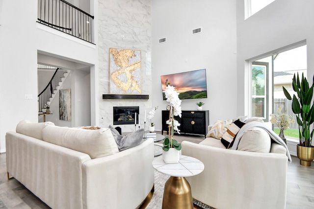 living room with a fireplace, light wood-type flooring, and a towering ceiling